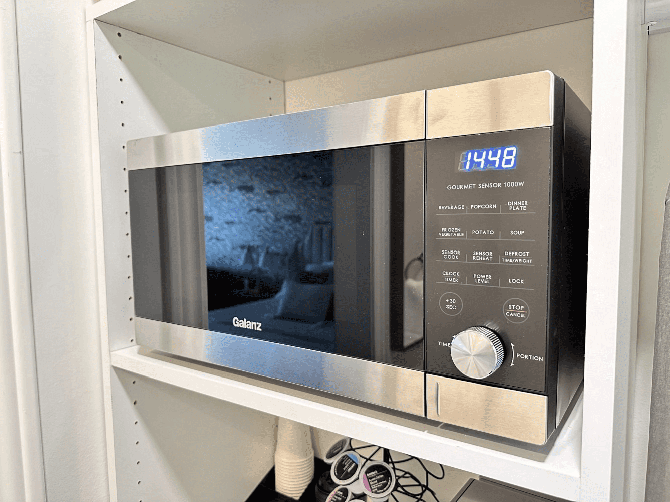 A stainless steel microwave oven is sitting on top of a white shelf.