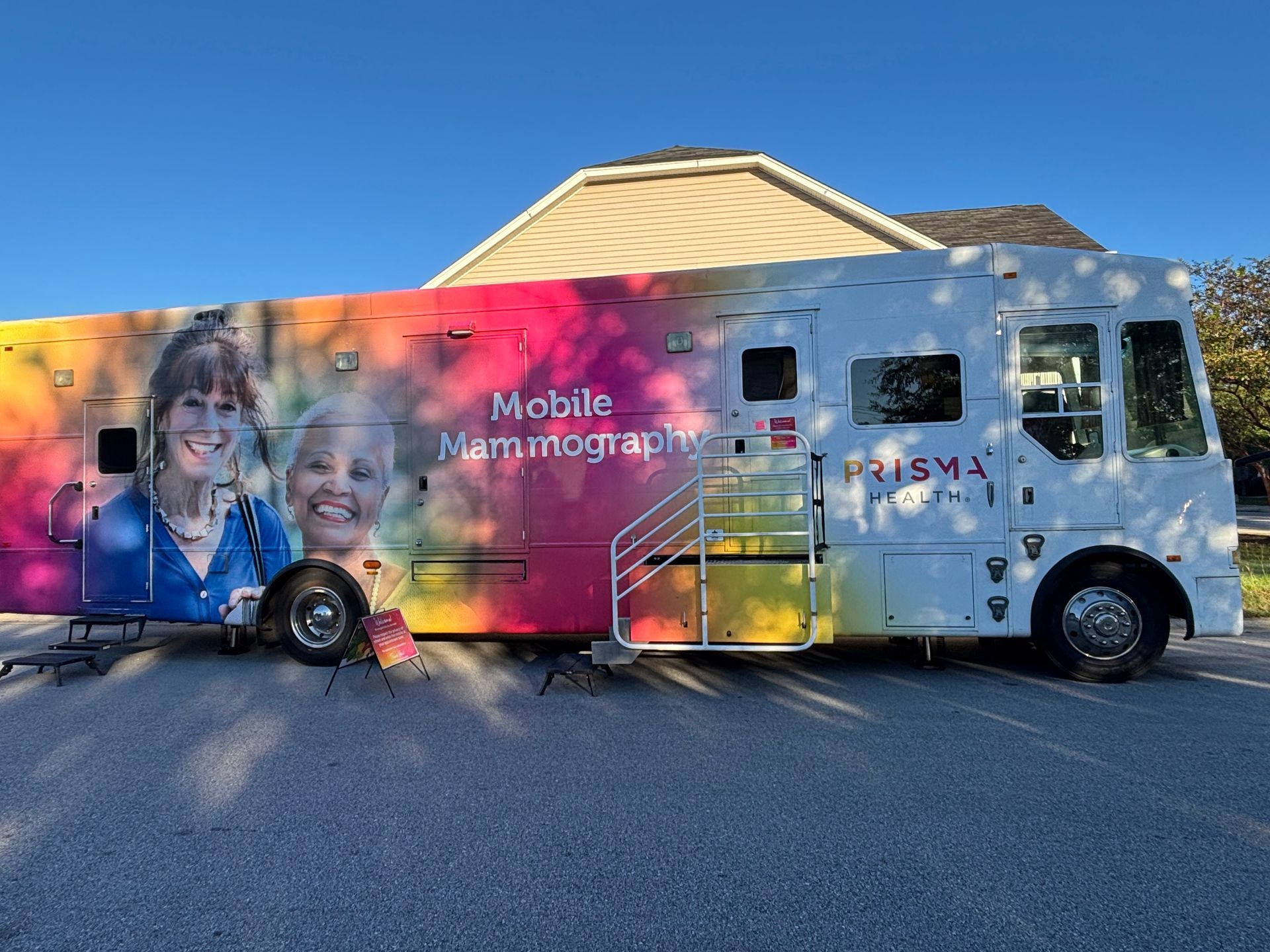 Mobile mammography bus with colorful wrap. Prisma Health logo. Stairs lead to the entrance.