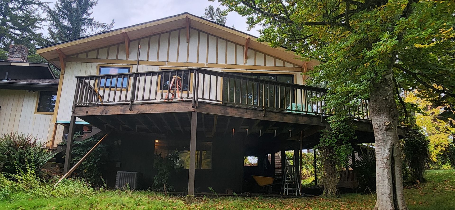 House with a large deck, surrounded by trees and greenery.