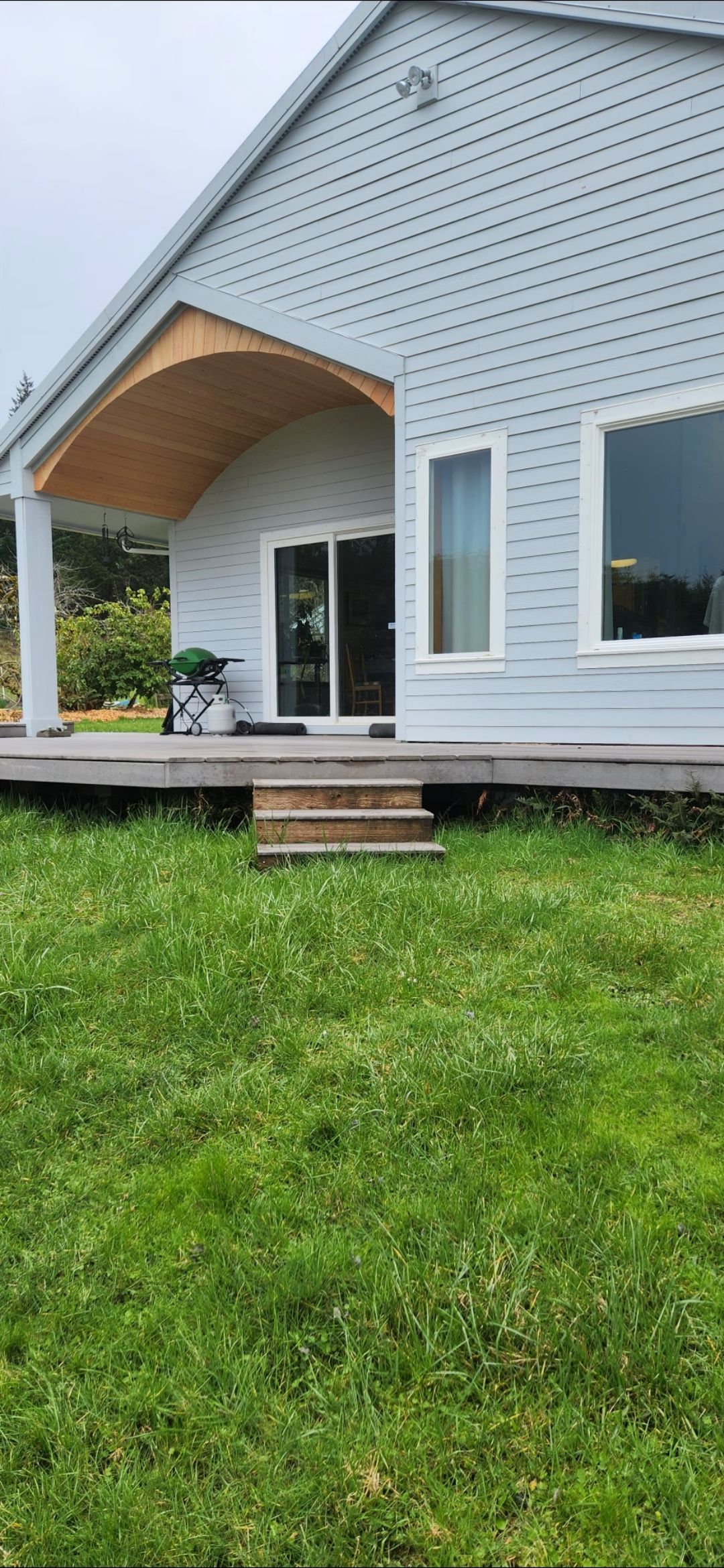 Light blue house with a wooden porch and steps, surrounded by green grass.