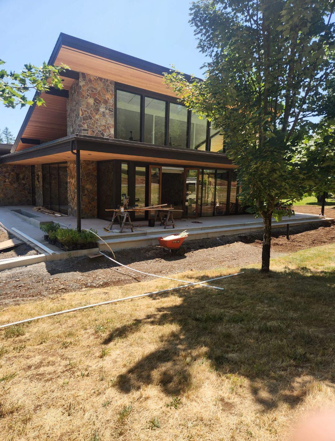 Modern house with stone facade, large windows, and a grassy yard under a bright sky.