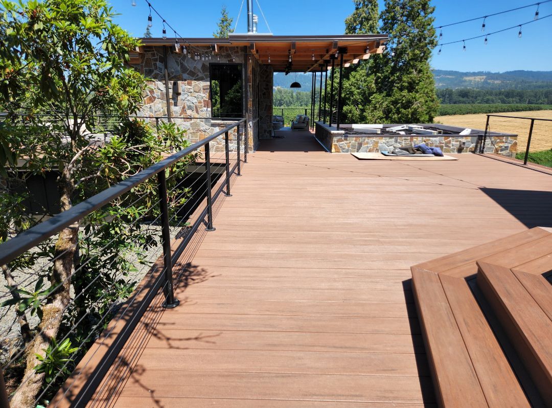 Wooden deck with railing, leading to a stone structure with a view of a field and trees.