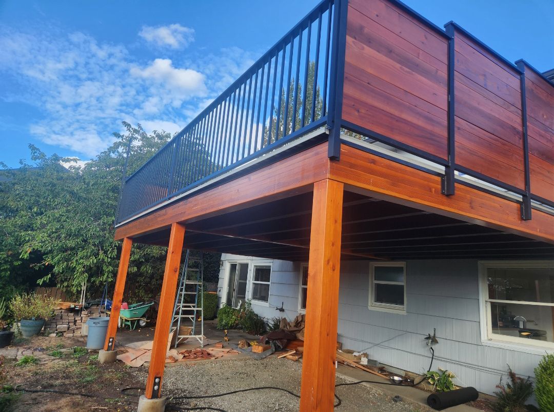 Wooden deck with black railing and wood-paneled privacy wall on a house, with wooden support posts.