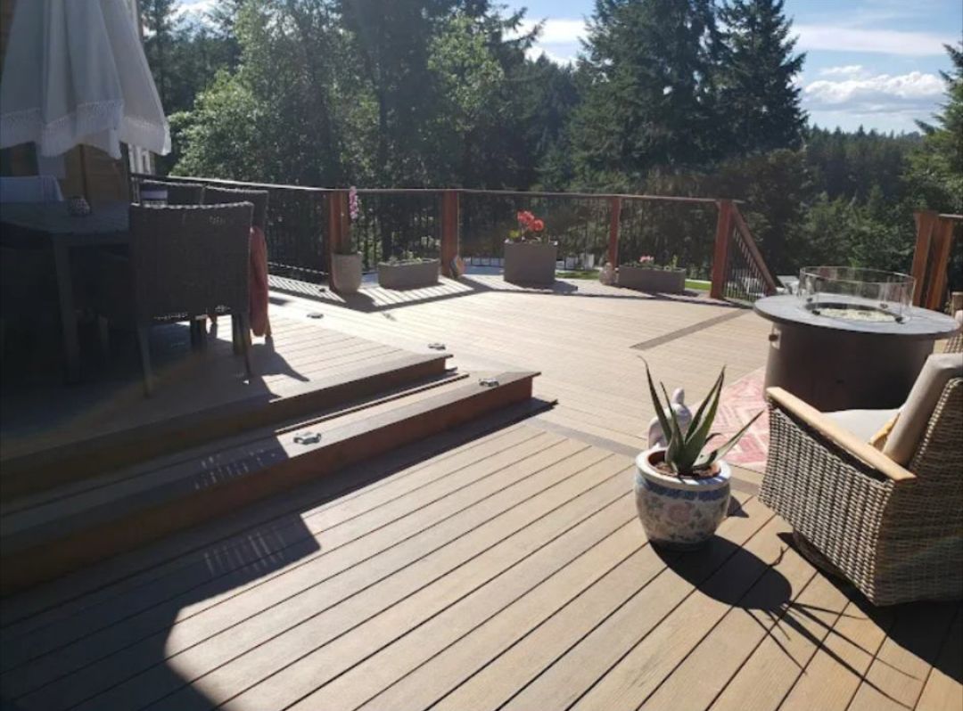 Wooden deck with seating and fire pit overlooking a forested area on a sunny day.