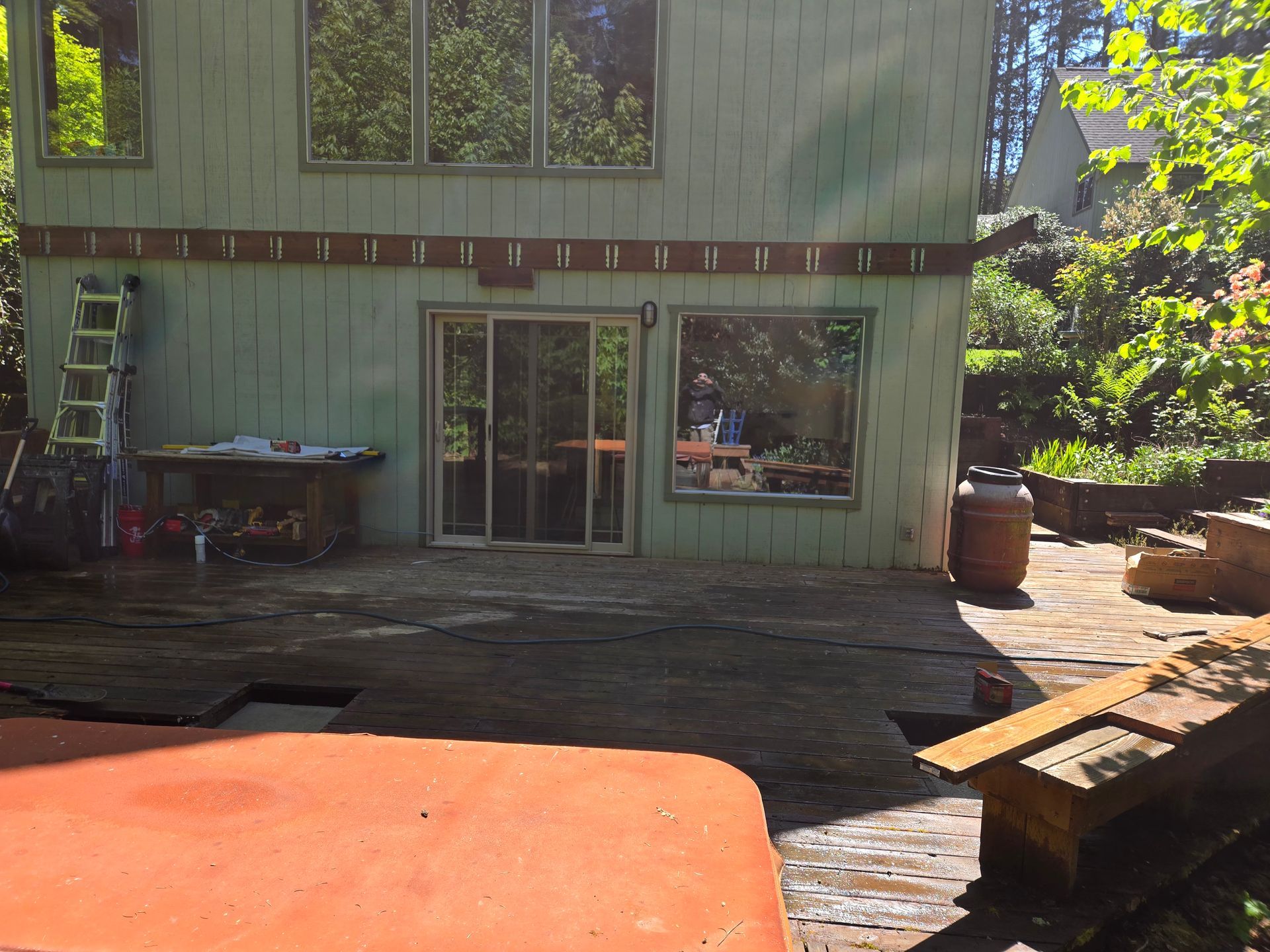 Green building with sliding door and deck. Partially constructed patio with a hot tub visible.