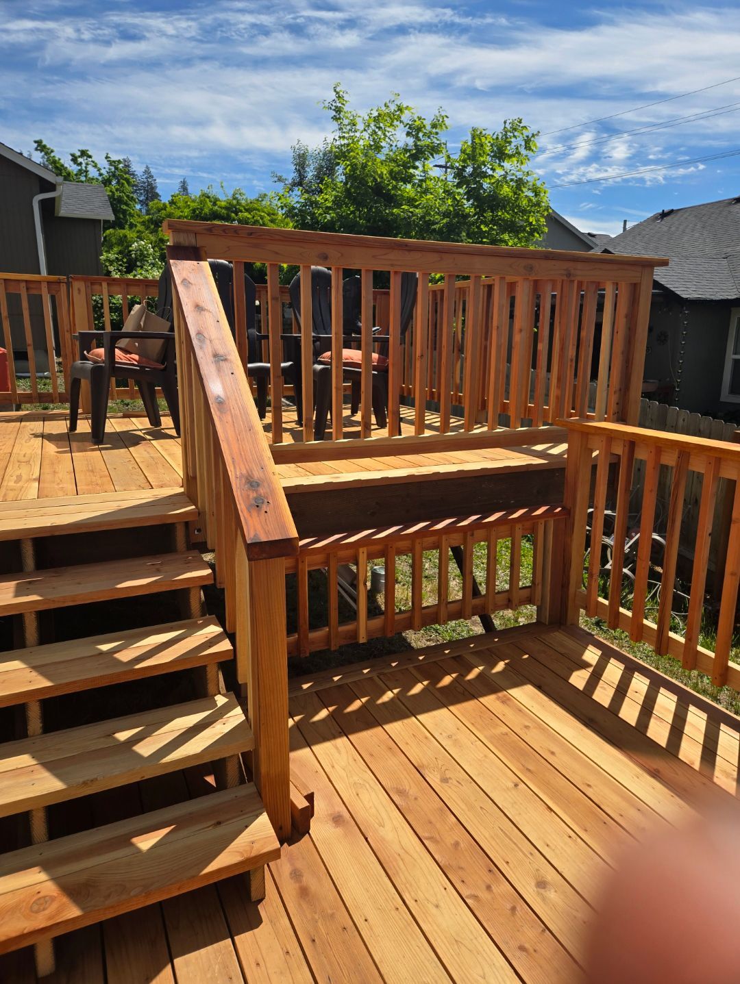 Wooden deck with stairs, railing, and chairs on a sunny day.