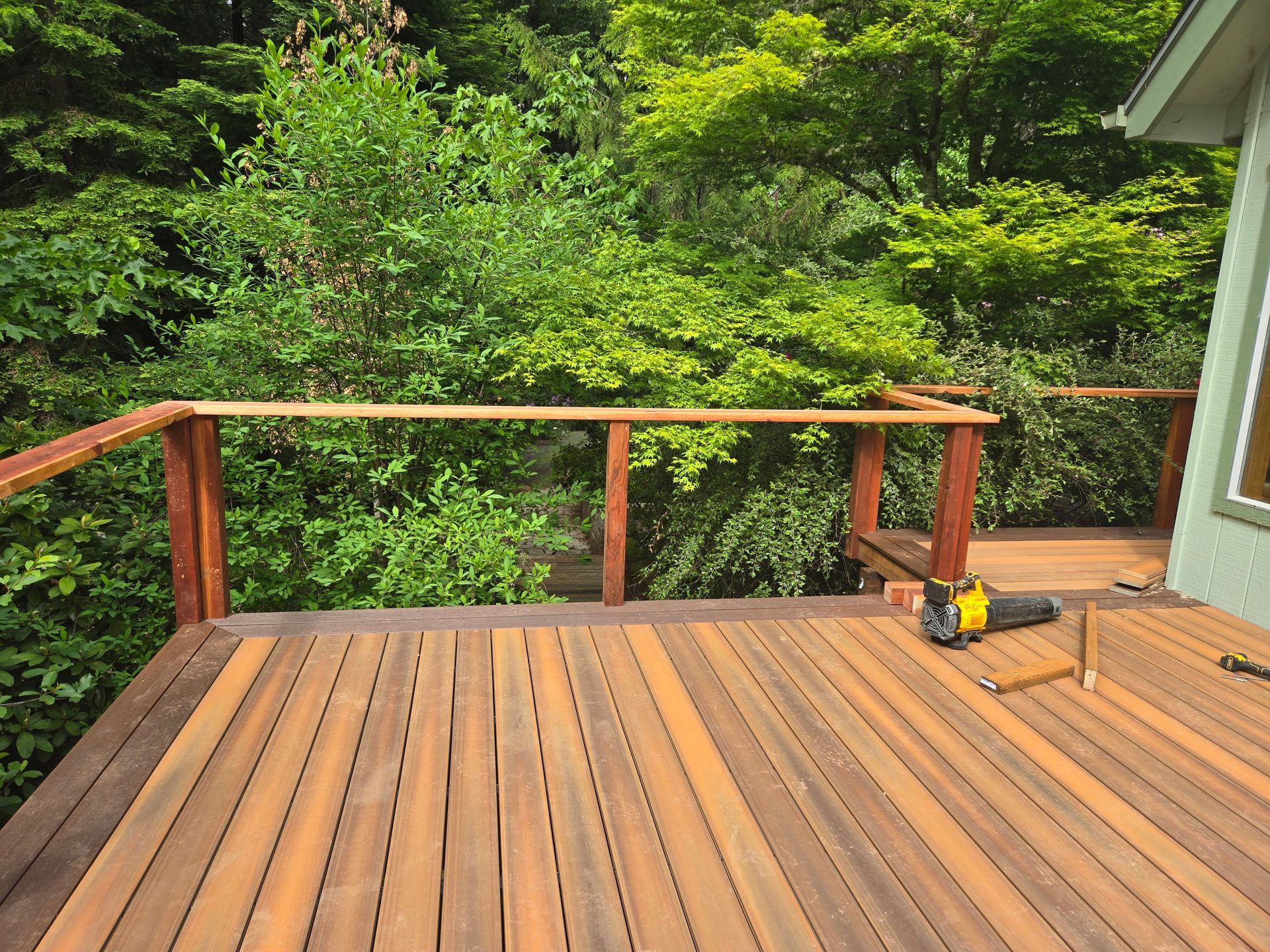 Backyard deck with wooden deck, and a green house with a sliding door.