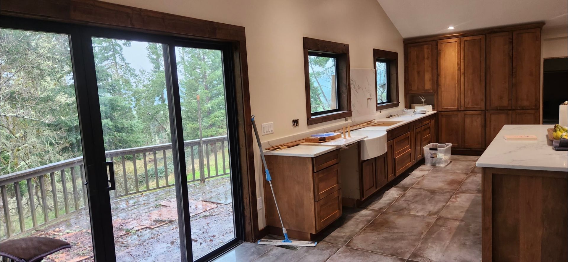 Kitchen with wood cabinets, light countertops, and a view of trees from a sliding glass door.
