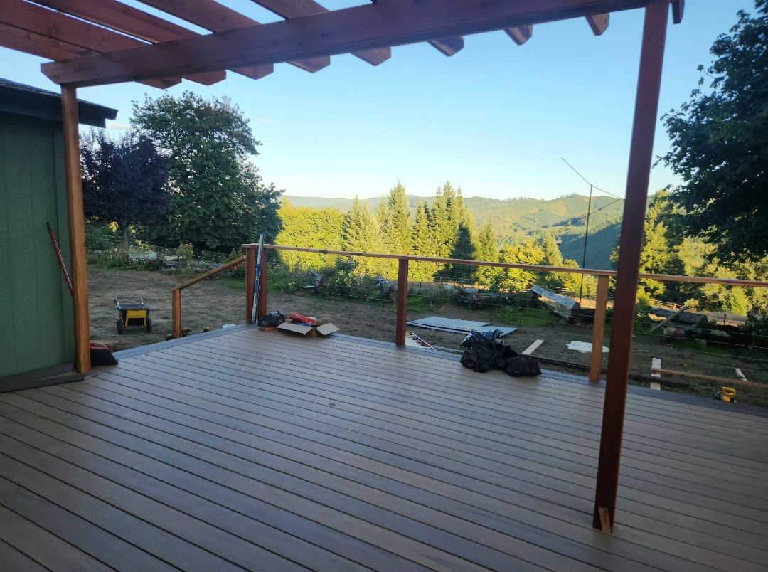 Wooden deck with pergola overlooking a lush, green valley under a bright sky.