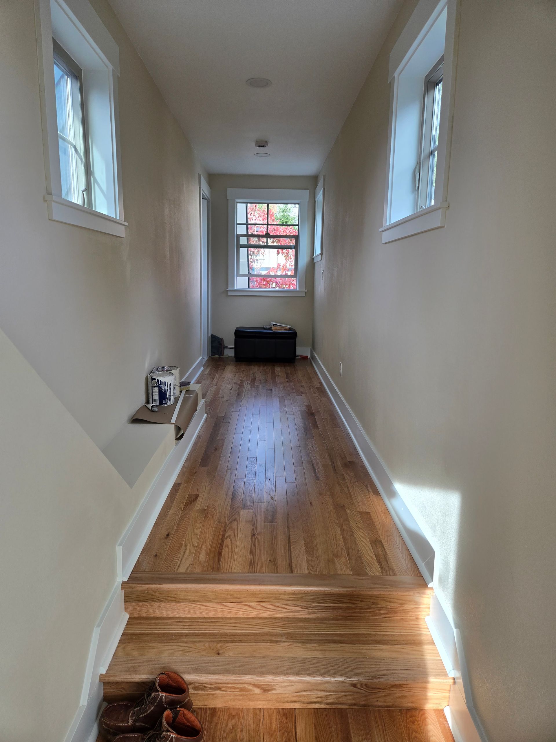 Hallway with hardwood floor, stairs, windows, and neutral walls.