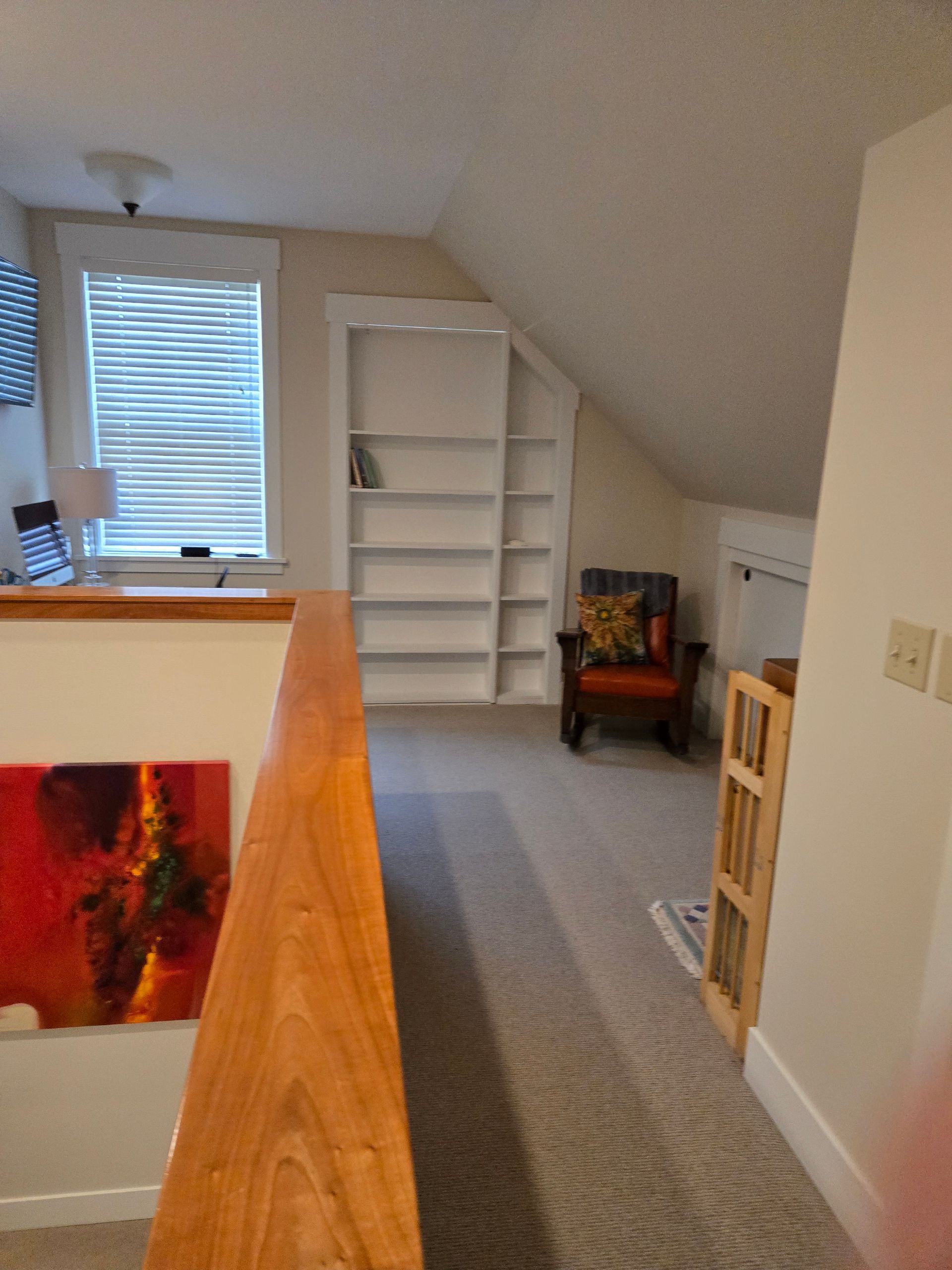 Loft space with built-in bookshelves, an armchair, and a railing. A window is in view.