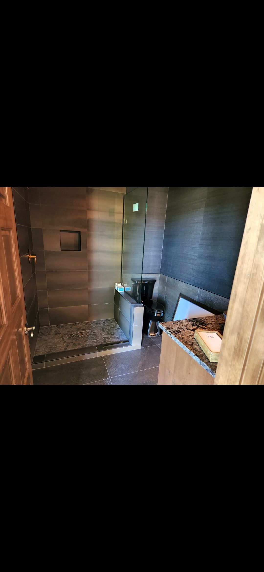 Green building with sliding door and deck. Partially constructed patio with a hot tub visible.