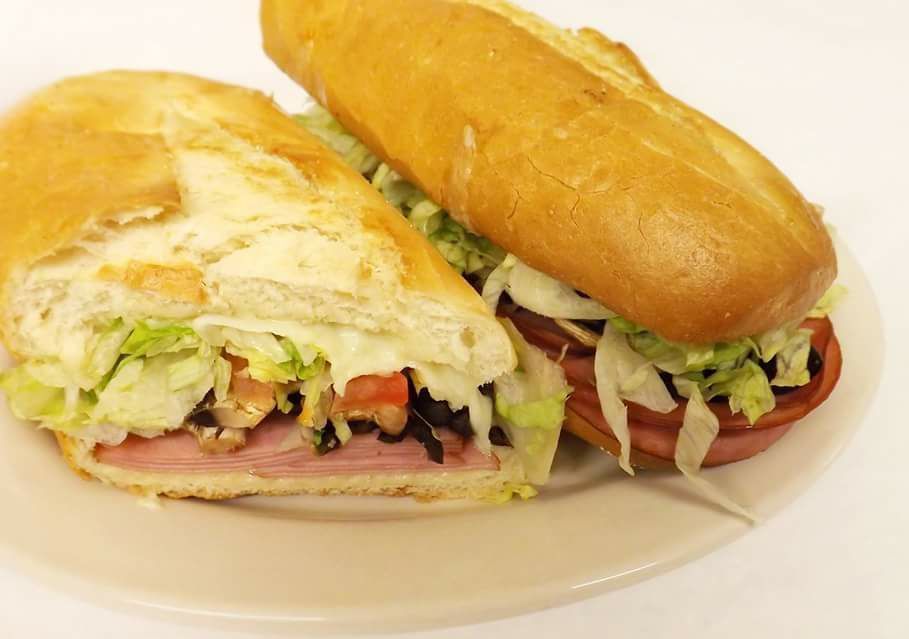 A grinder sandwich with lettuce tomatoes and ham on a white plate.