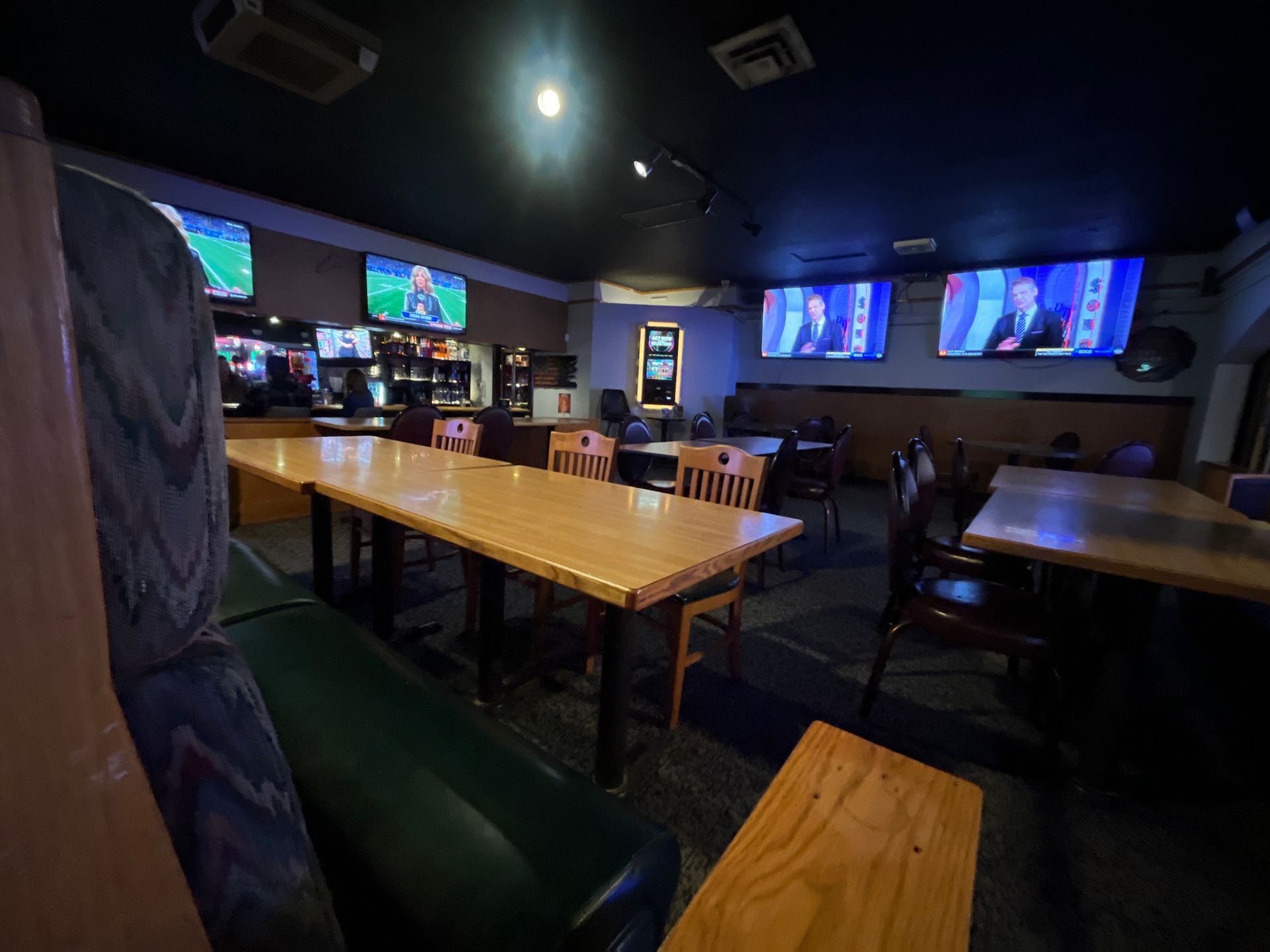 A restaurant bar with tables and chairs and televisions on the wall.