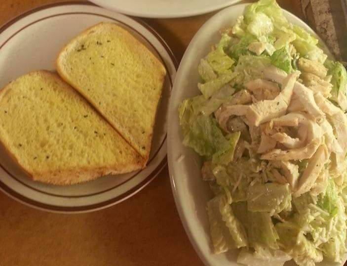 A plate of chicken caesar salad next to a plate of garlic bread
