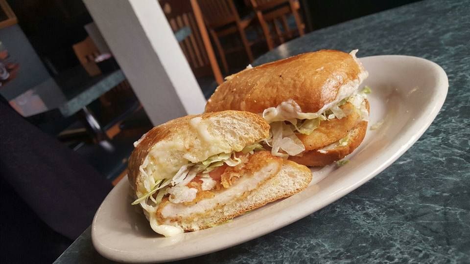 A chicken sandwich is on a white plate on a table.