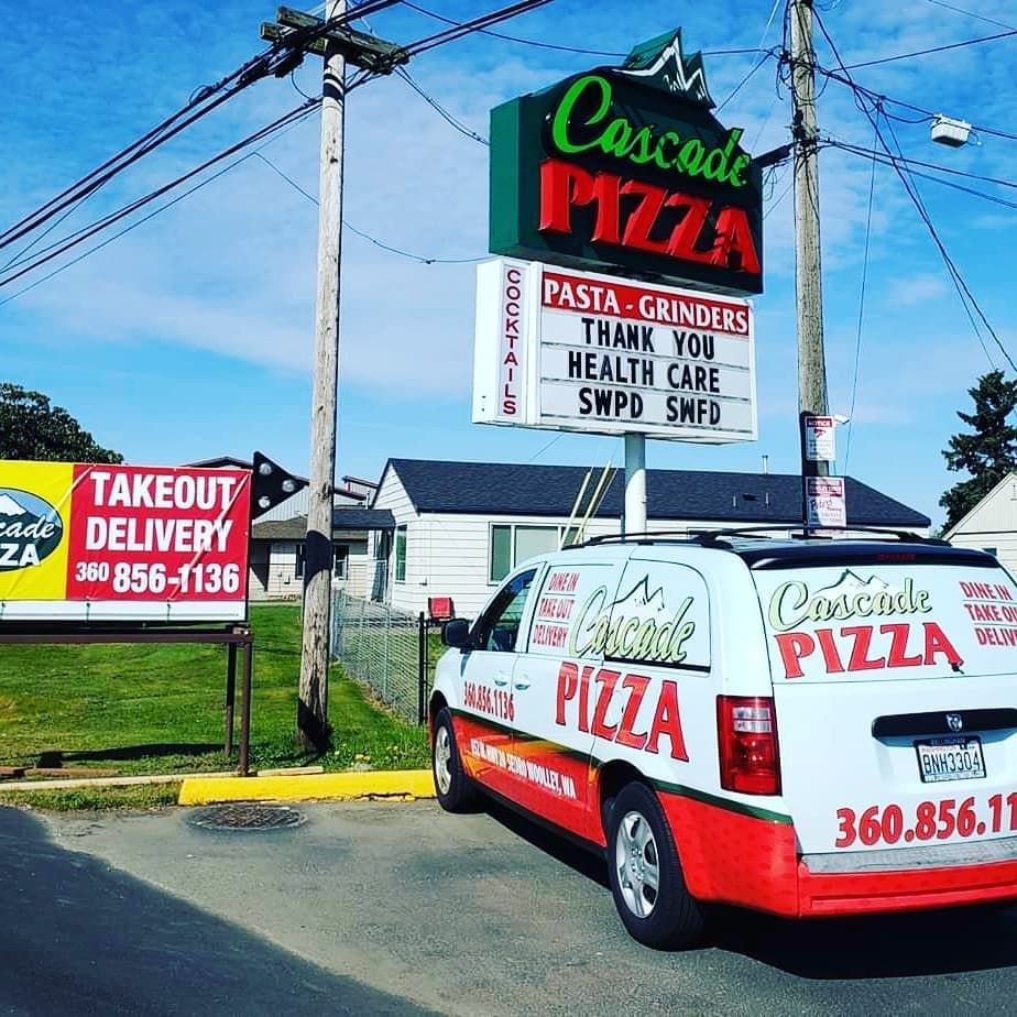 A white pizza delivery van is parked in front of a sign for cascade pizza in Sedro-Woolley, WA