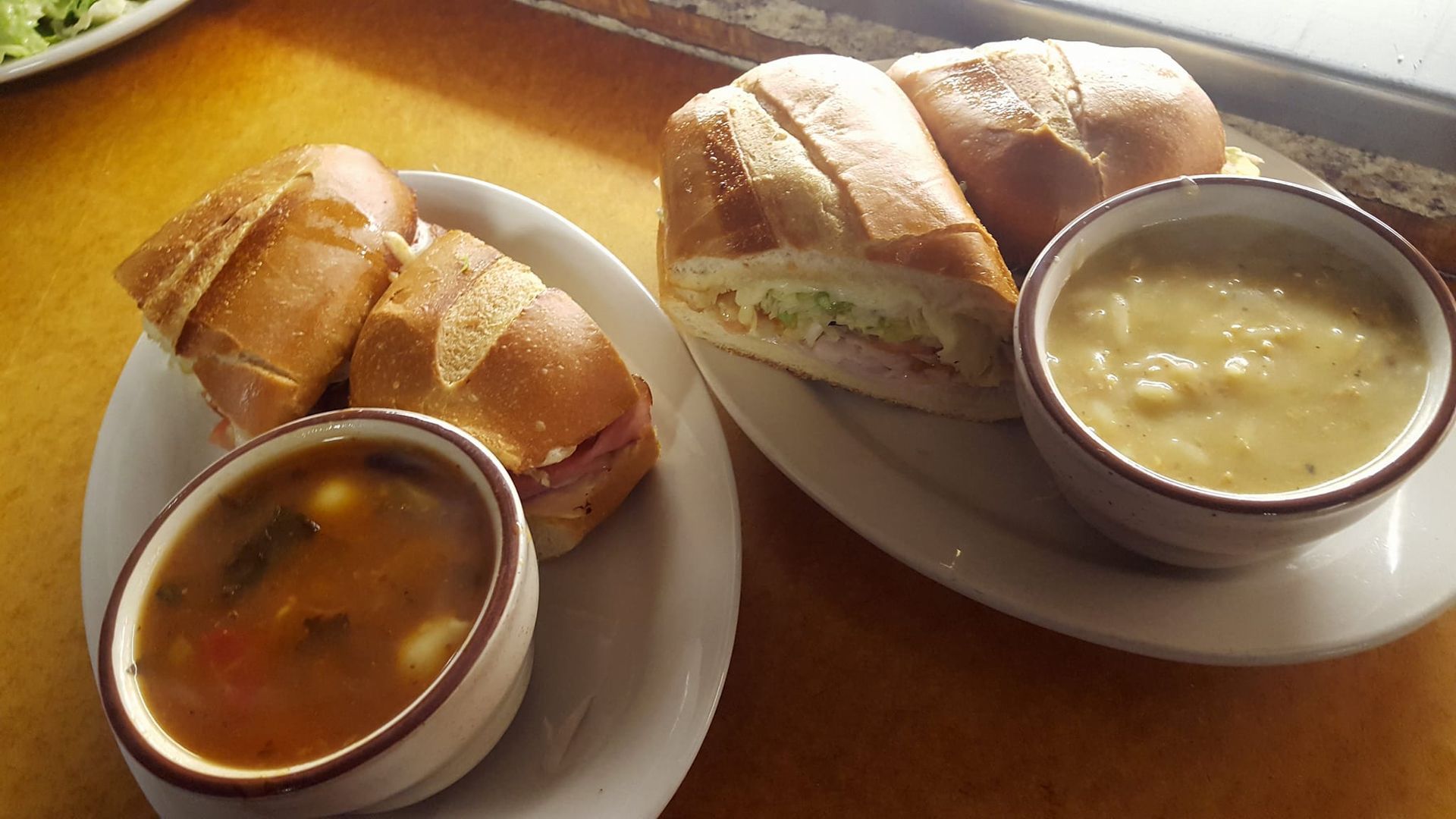 Two sandwiches and two bowls of soup on plates on a table