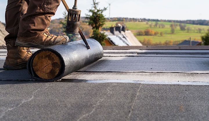 a man is rolling a roll of roofing material on a roof .