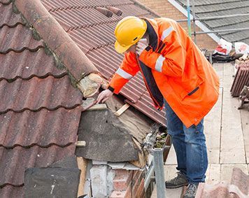 a man in an orange jacket and hard hat is working on a roof .