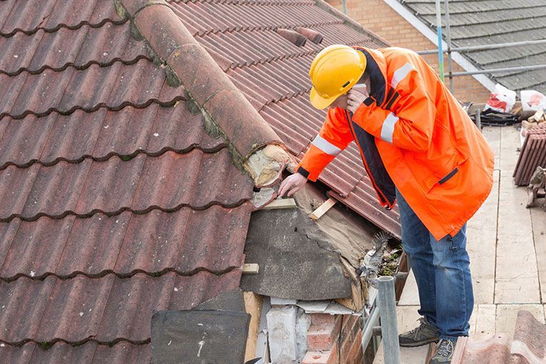 a man in an orange jacket and hard hat is working on a roof .