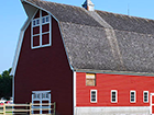 a red barn with a gray roof and a fence in front of it .