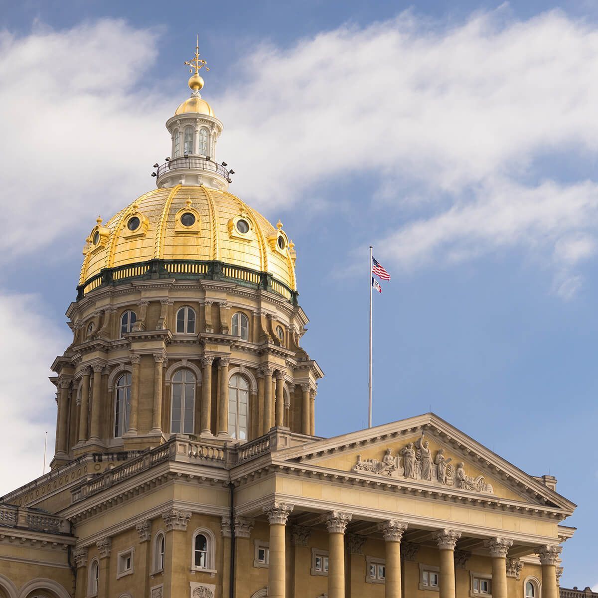 Iowa State Capitol building with gold dome and US flag.