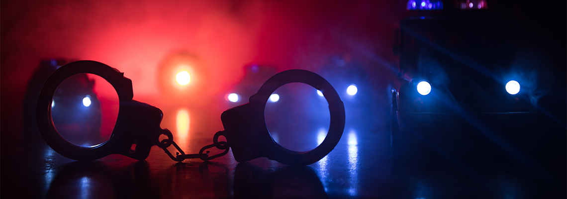 Handcuffs sit in front of red and blue emergency lights with smoke in a dark setting.