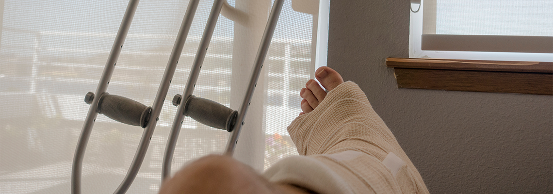 Foot in a cast with crutches next to it, indoors near a window.