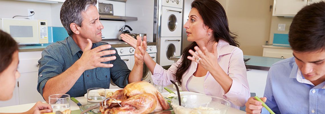 Family arguing at the dinner table. Mom and dad gesturing, son looking down, turkey and food.