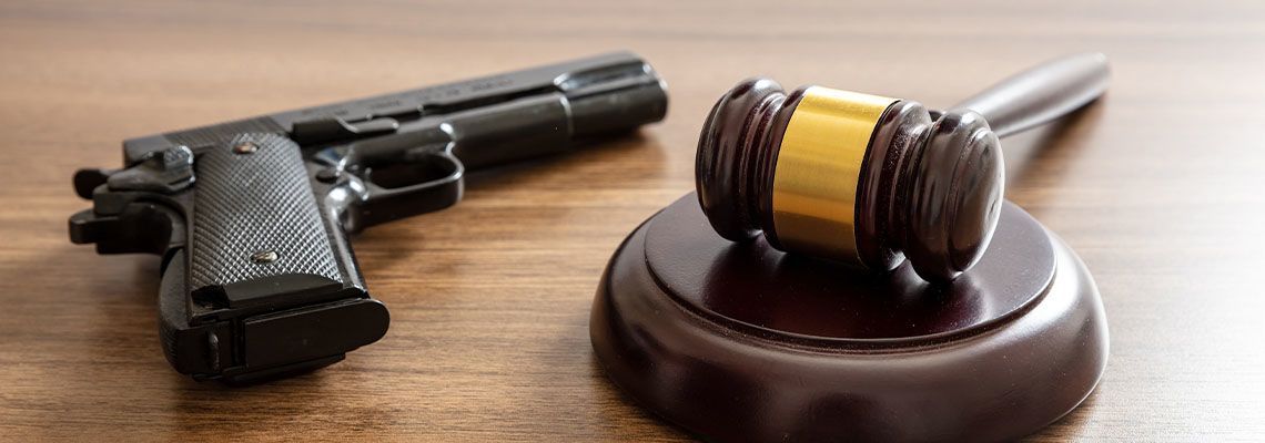 A handgun and a gavel on a wooden surface, implying legal or judicial context.