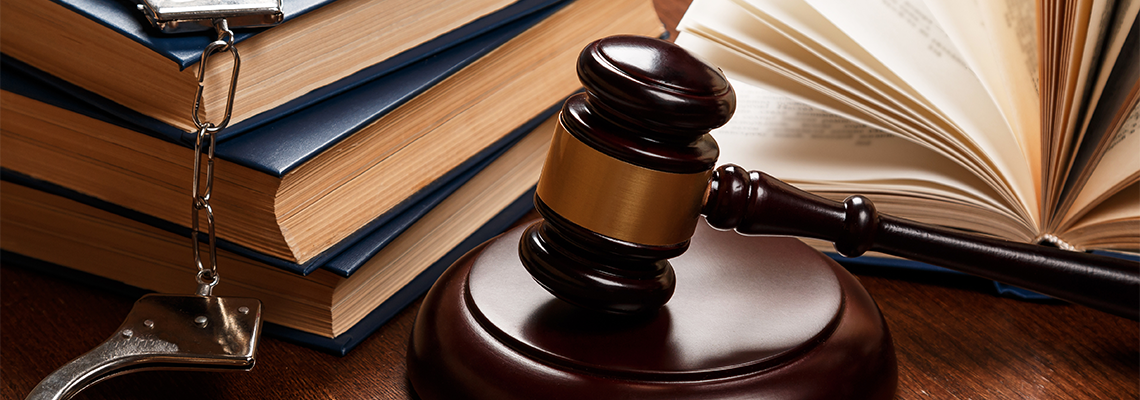 Gavel on a wooden block next to a stack of books with handcuffs in the frame.