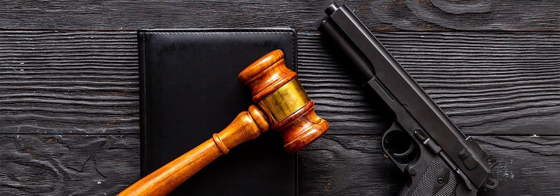 A gavel, a black handgun, and a book rest on a dark wooden surface.