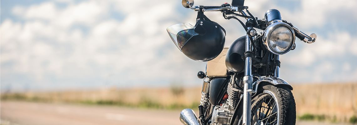 Motorcycle with black helmet hanging on handlebars parked on a road with a cloudy sky.