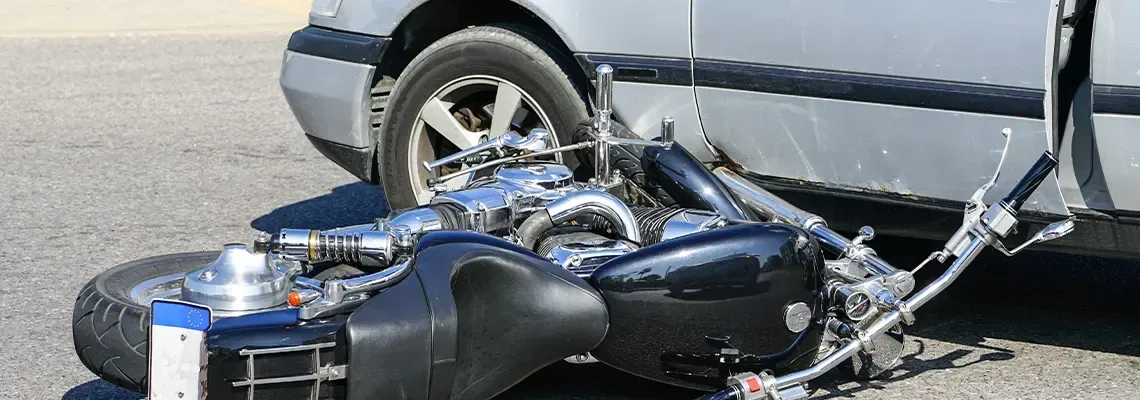 Motorcycle crashed under car, on pavement.