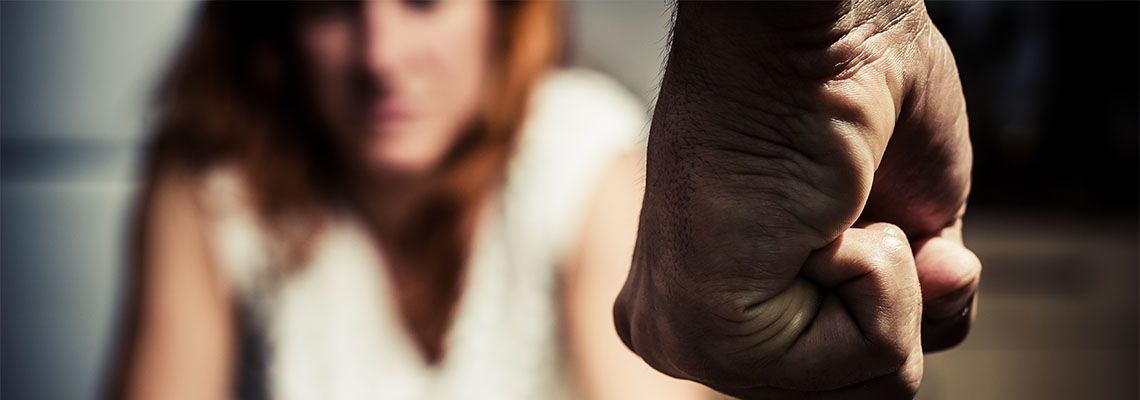 A clenched fist in the foreground with a woman in the blurred background.