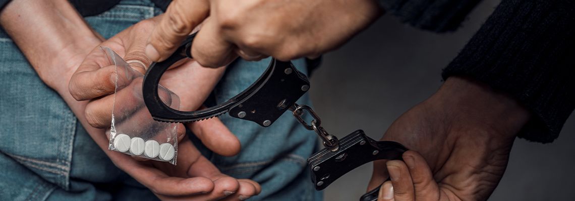 A person is being handcuffed with drugs in their hand.