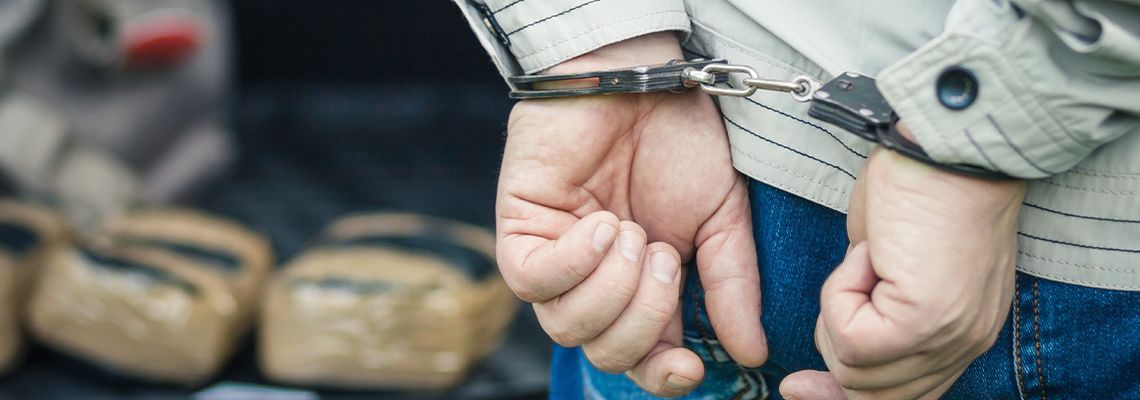 Person in handcuffs; bags in the background.