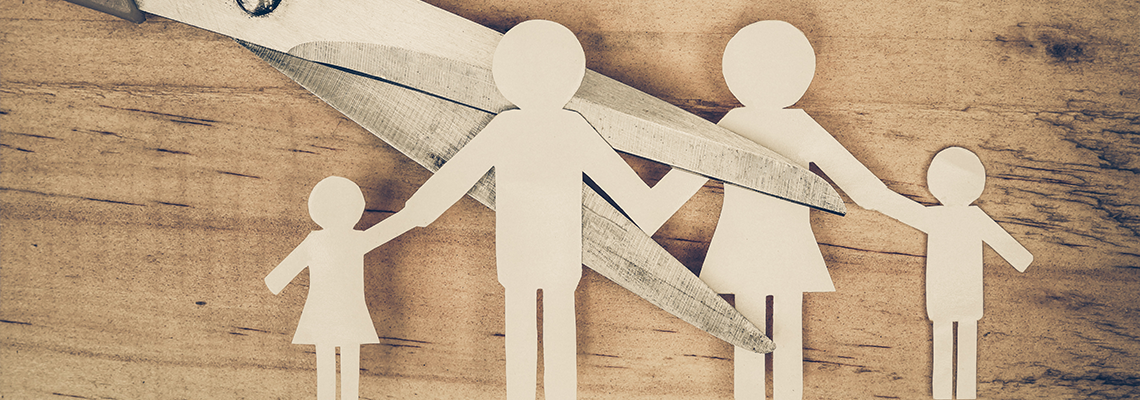 Scissors cutting a paper family, representing family separation or divorce on a wood background.