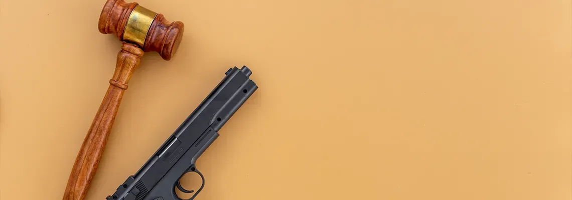 A wooden gavel and a handgun on a beige surface.