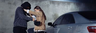 A hooded person appears to be robbing a woman near a car at night.