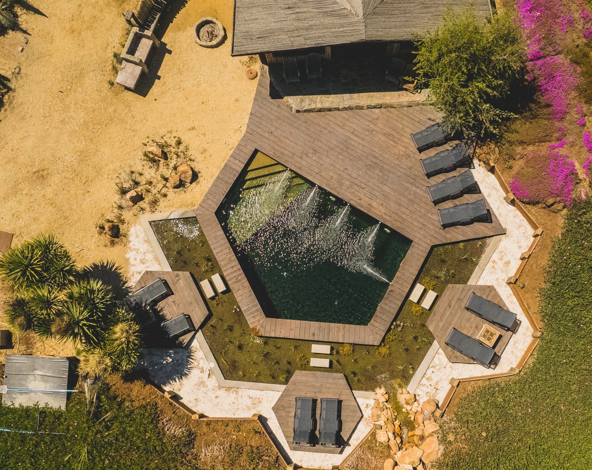 Overhead view of a hexagonal pool with wooden deck and lounge chairs surrounded by landscaping.