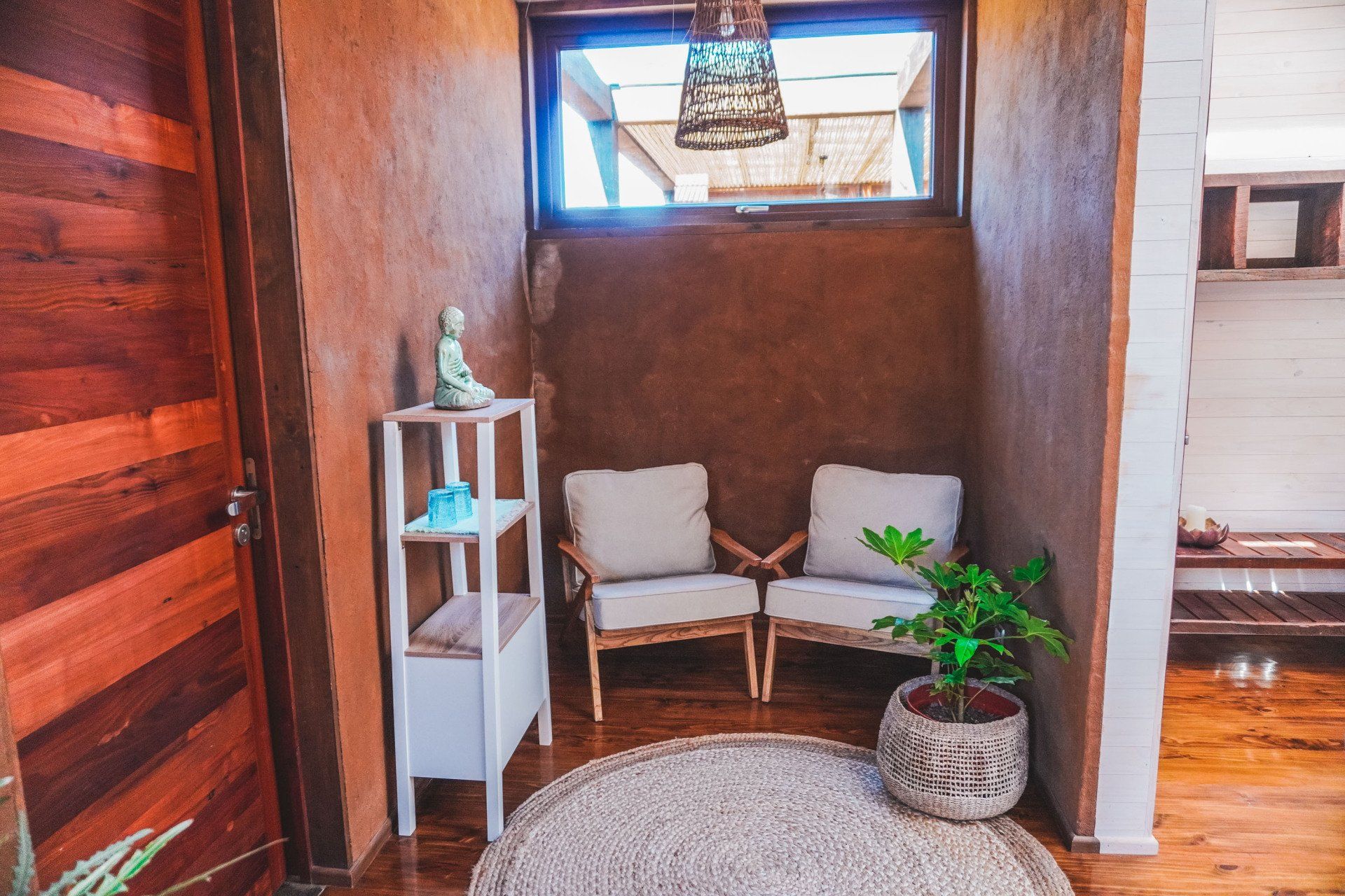 Cozy waiting area with two chairs, a plant, and a small shelf, lit by natural light.