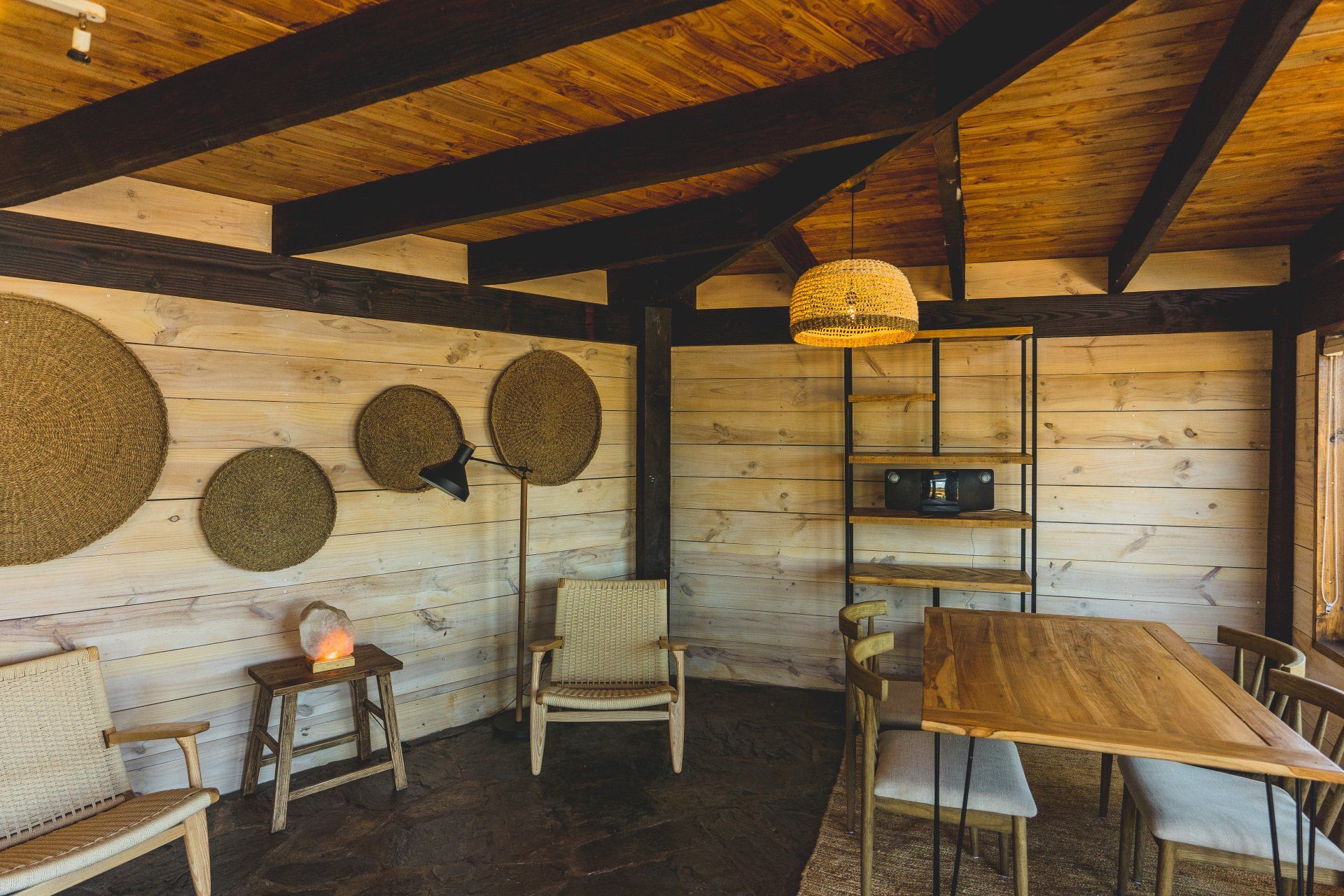 Wooden interior with a dining table, chairs, and decorative wall hangings.