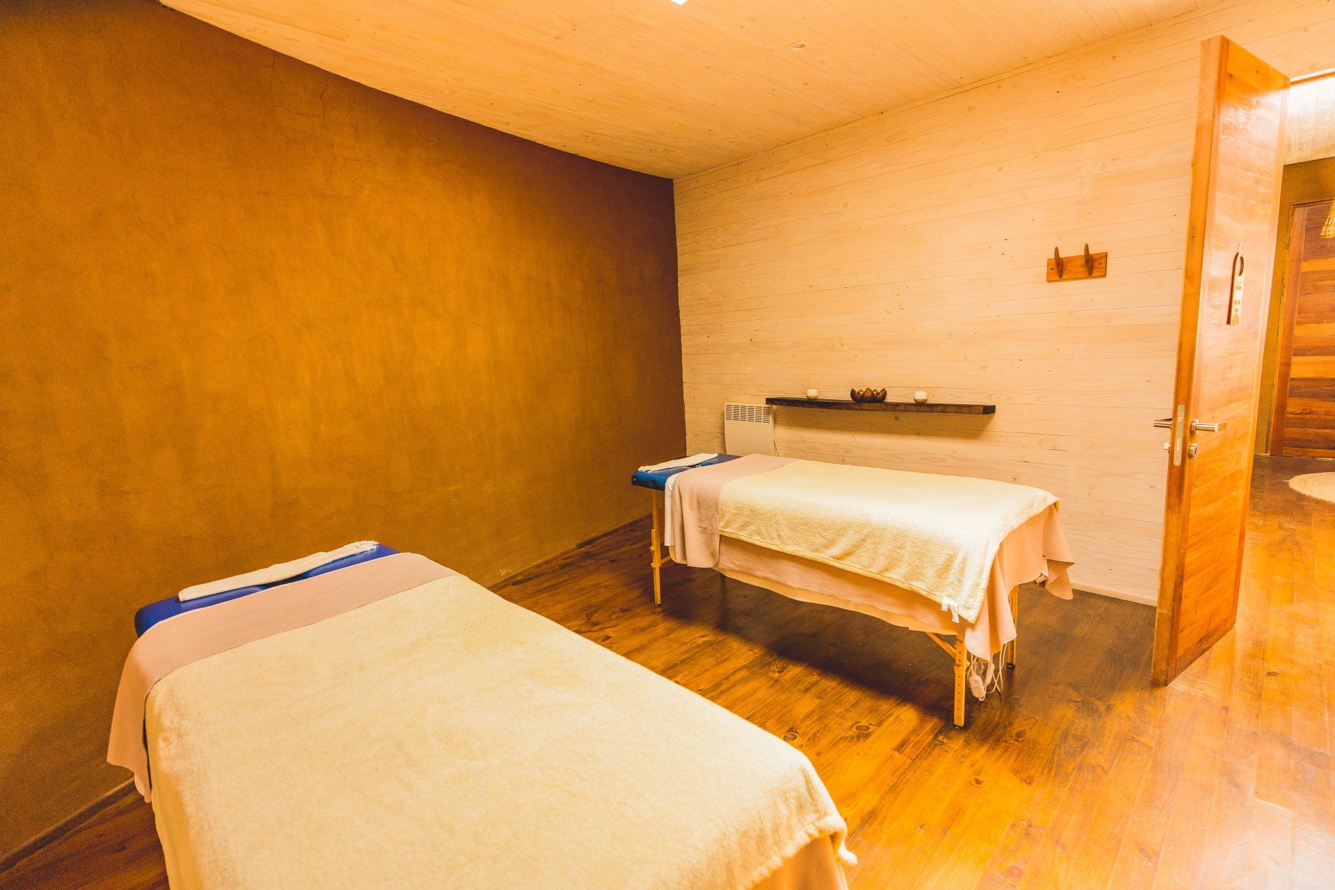 Two massage tables in a spa room with beige walls and wood flooring.