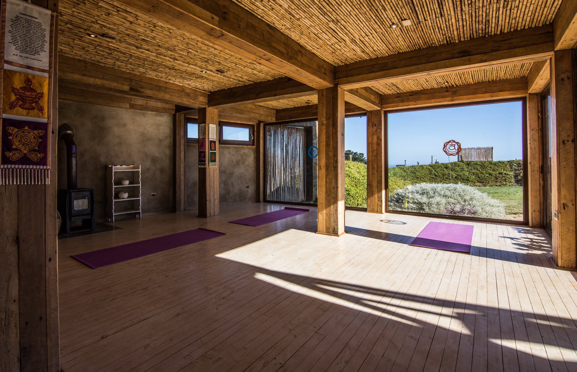 Yoga studio with open windows, wooden beams, mats, and a view of greenery.