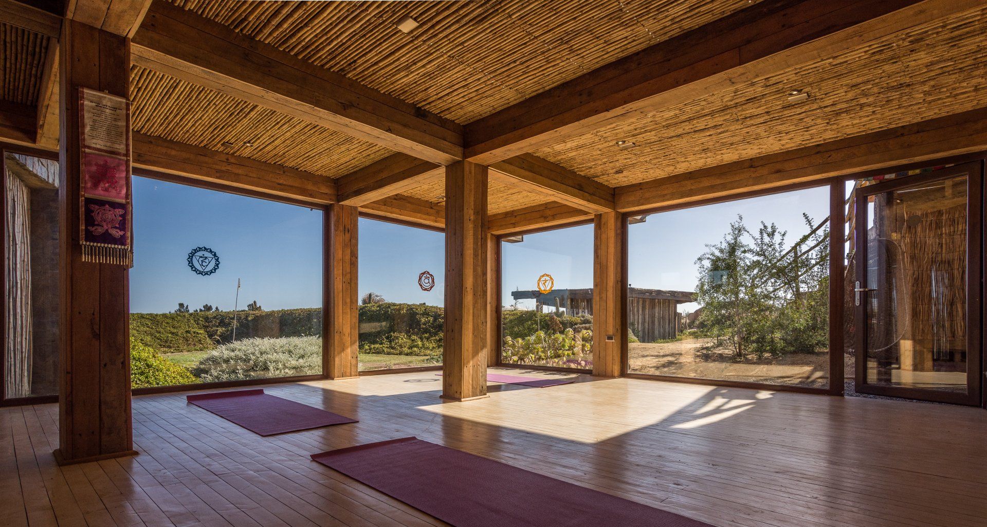 Yoga studio with wood beams, large windows overlooking outdoor greenery, and yoga mats.