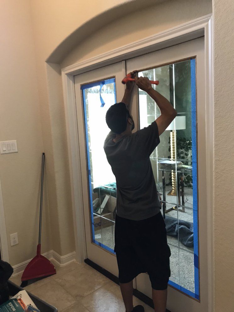 Person using a tool on a glass door, applying tape. Interior view with a broom and other items visible.