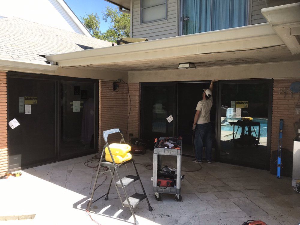 Man working on sliding glass doors on a patio with a ladder and tools.