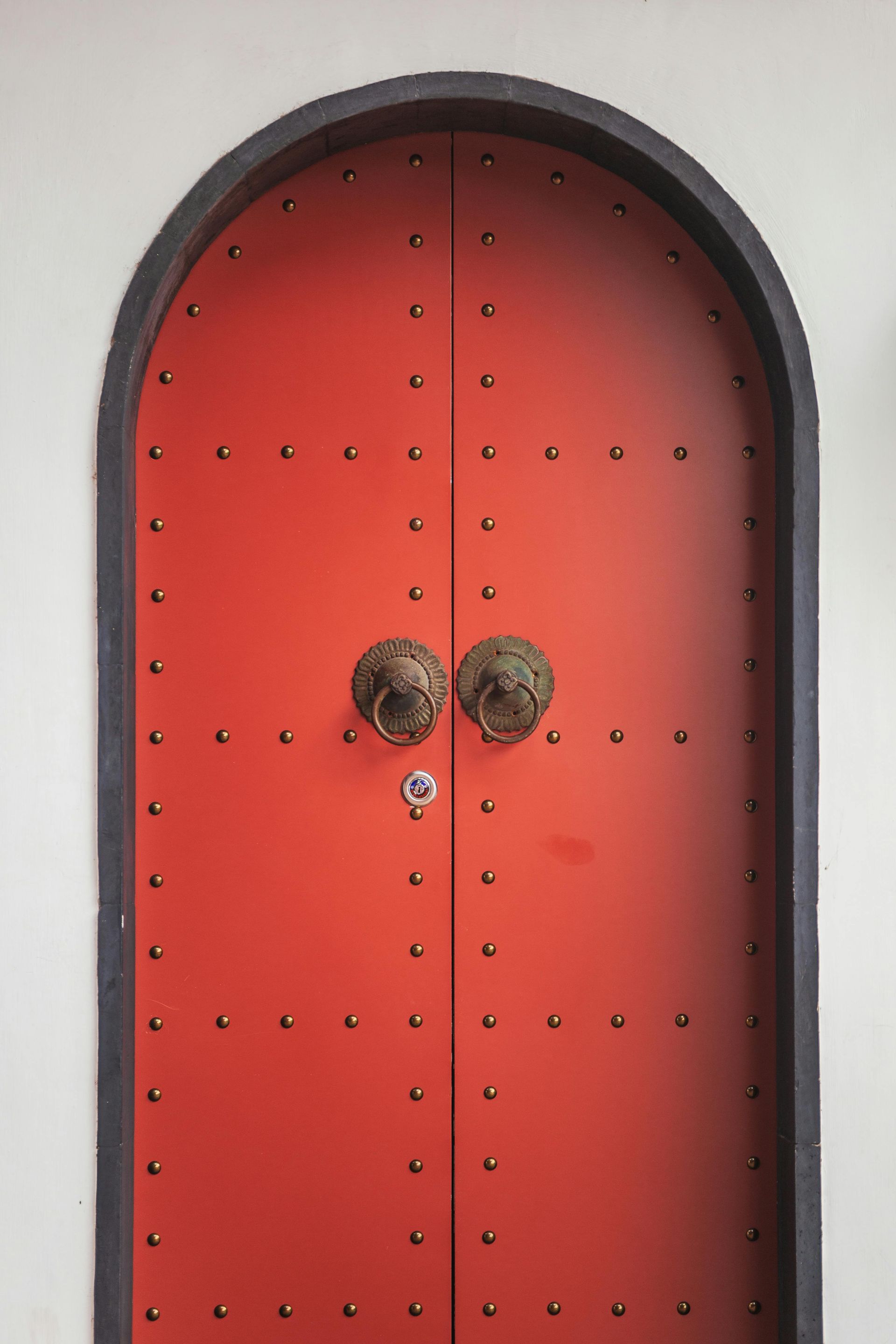 Red arched door with brass lion-head door knockers and black trim.